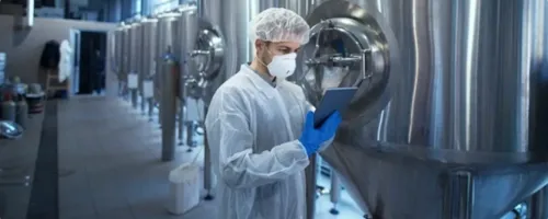 Factory worker wearing safety gloves, mask and hair net, checking a computer tablet.