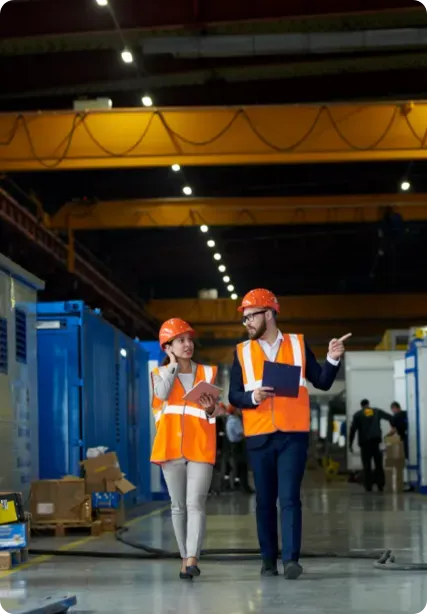 Man and woman in a warehouse wearing orange PPE.