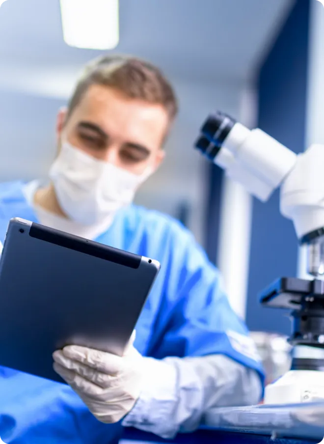Scientist using a tablet in front of a microscope.