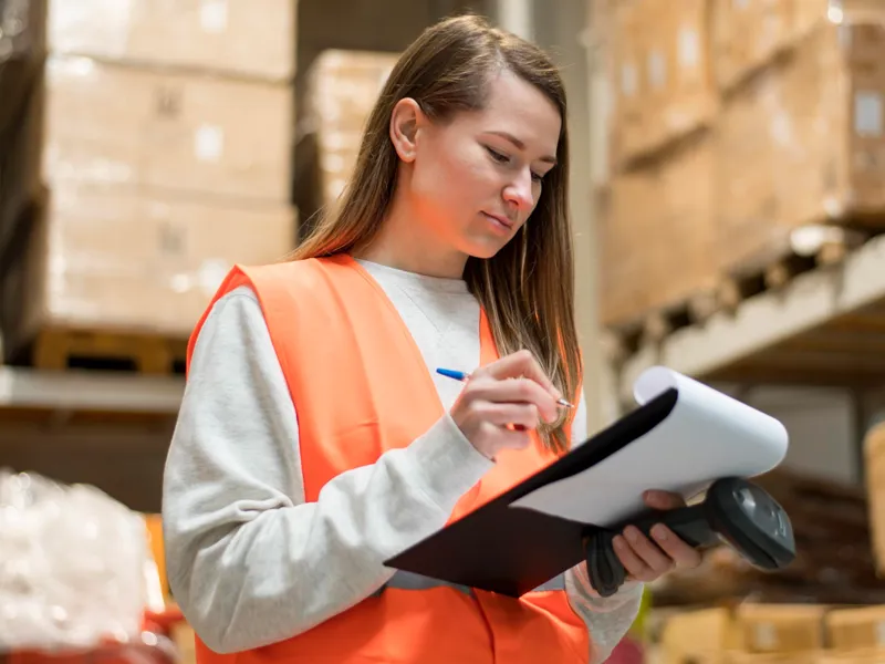 A warehouse worker checks a document on a clipboard