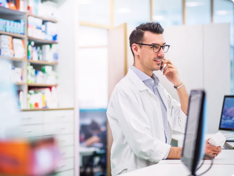 A pharmacist behind a counter, talking on the phone.