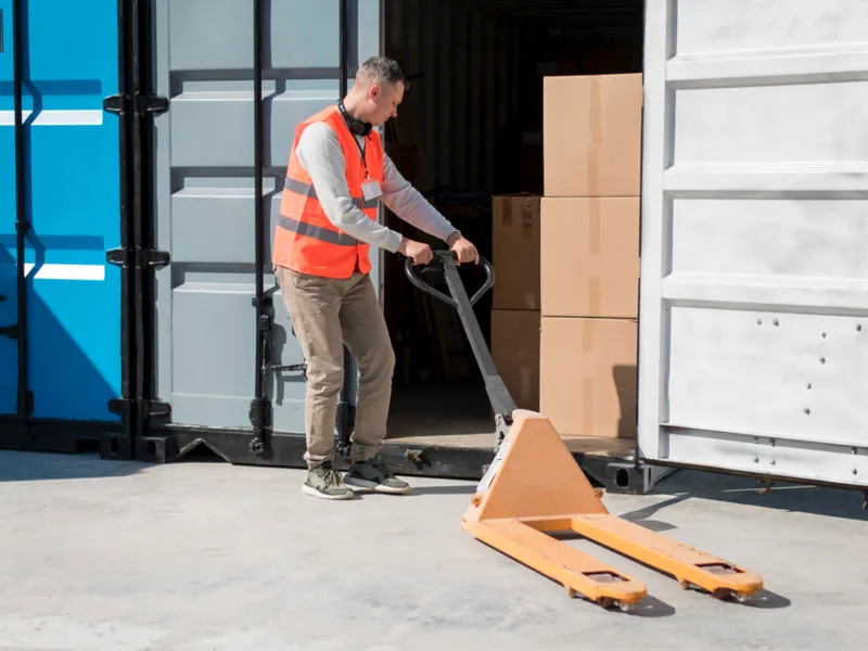 A worker wheels a dolly up to a storage container
