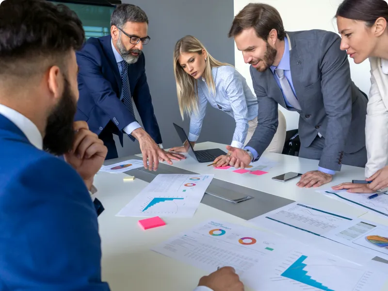 A group of people study paper graphs set out on a table